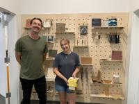 Picture shows two individuals a part of the exhibition posing in front of the eco materials 